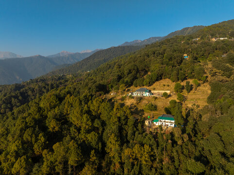 Aerial view of houses nestled amidst the lush green hills, with the clear blue sky creating a serene contrast, Bir, Himachal Pradesh, India. - Powered by Adobe