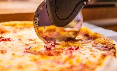 Sharp pizza cutter slicing hot cheese pizza in warm kitchen lighting.
