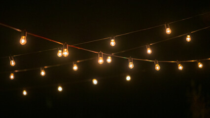 String of warm glowing light bulbs hanging in dark night.