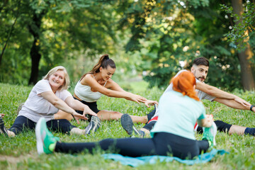 Group of people stretching in a park during a fitness class on a sunny day