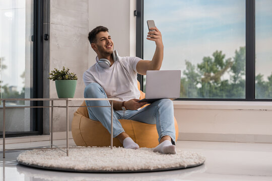 Young man enjoys taking a selfie while working on his laptop in a bright and modern indoor space