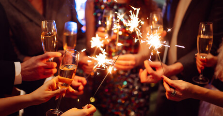 Hands hold sparklers, creating bright sparks in a lively setting. Friends celebrate together as...