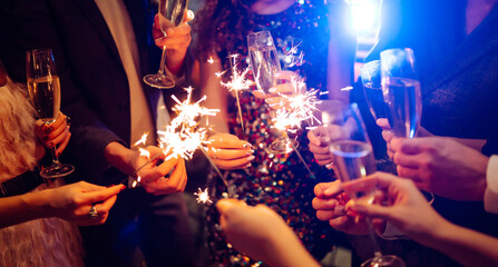 Fototapeta na wymiar Hands hold sparklers, creating bright sparks in a lively setting. Friends celebrate together as lights twinkle and laughter fills the air during a special event.