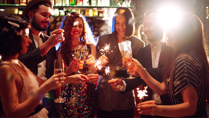 Fototapeta premium Friends gather at a vibrant bar to celebrate New Year's Eve. They enjoy drinks while holding sparklers, surrounded by a festive atmosphere and sparkling decorations.