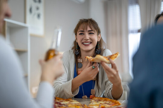 Laughing young woman enjoying pizza with friends in a cozy indoor setting during a casual gathering
