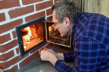 Wood stove heating country house middle aged man maintains fire brick wood burning stove.