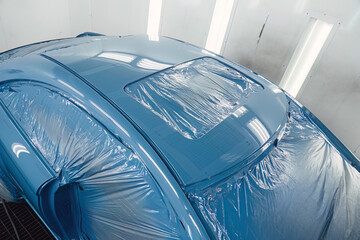 Technician preparing a modern car for paint, carefully masking the body with specialized film...