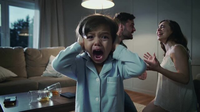 Scary afraid child boy close ears while his parent are having a fight in the living room. Sad depressed child feeling lonely. domestic violence concept