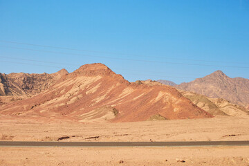 Obraz premium Desert landscape featuring rugged mountains under a clear blue sky with a winding road