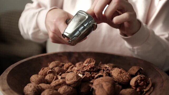 Closeup video of cracking walnuts using special tool. Nuts in a vintage wooden bowl. Healthy snack rich in fiber, fat and nutrients. Removing shell from walnuts. 