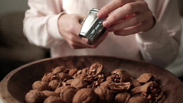 Closeup video of cracking walnuts using special tool. Nuts in a vintage wooden bowl. Healthy snack rich in fiber, fat and nutrients. Removing shell from walnuts. 