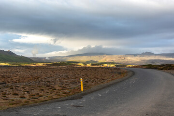 Icelandic landscape with asphalt road and mountains in cloudy weather.