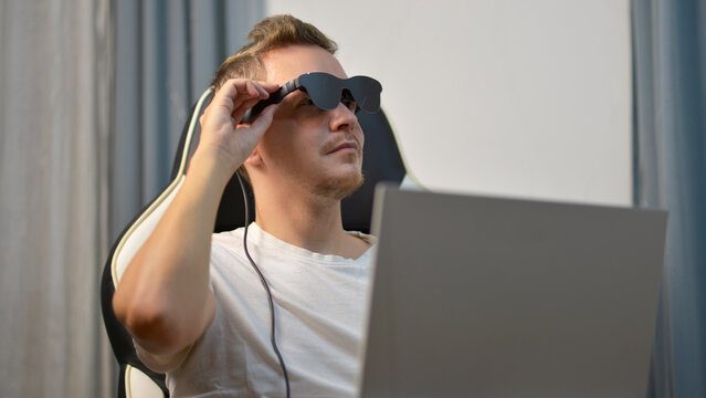 Man Putting On Wearable AR XR Smart Glasses While Using Laptop