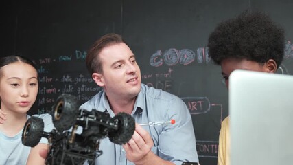 Smart teacher inspect car model construction to diverse student. high school children with mixed races listening mentor explain robotic model system at table with laptop and wires placed. Edification - Powered by Adobe