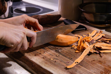 Cutting a peeled sweet potato in half on a wood cutting board
