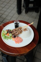 Delicious Balinese Sate Lilit with Rice and Sambal Matah Ready to Eat on a Round Wooden Table for a Flavorful Meal Experience, Perfect for Food Blogs