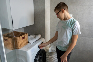 Boy with glasses setting washing machine program by turning dial knob in modern bathroom at home. Cildren learning to use household appliances, independence training and life skills education.