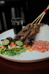 Delicious Asian-inspired satay skewers plated with rice, chili relish, and vibrant salad for a flavorful dining experience in a modern setting