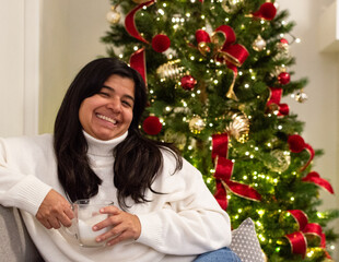 Smiling Woman Sitting by Decorated Christmas Tree.