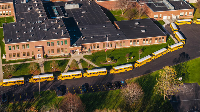 Aerial view of a typical American school with a long row of yellow school buses lined up outside the building on a sunny autumn day.