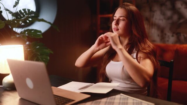 An woman works on her laptop in a cozy home she suddenly feels pain in her neck and back stretching uncomfortably her tense expression shows discomfort from long hours of remote work