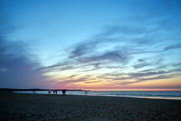 Obraz premium Blurred silhouettes of people walking on a sandy beach by the Baltic Sea in the evening