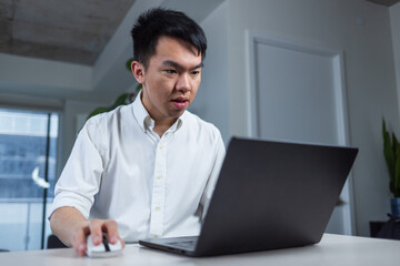 Young man focuses on his laptop while working from home. Clean indoor setup showing concentration and modern remote work.