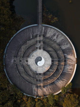 Aerial view of a circular structure featuring a yin and yang symbol, surrounded by water and trees, casting long shadows in the fading light, Hangzhou, Zhejiang, China.