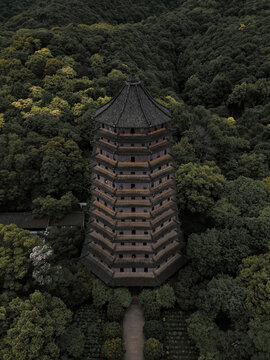Aerial view of the Leifeng Pagoda standing tall amidst a dense forest, its dark silhouette contrasting with the surrounding verdant canopy, Hangzhou, Zhejiang, China.
