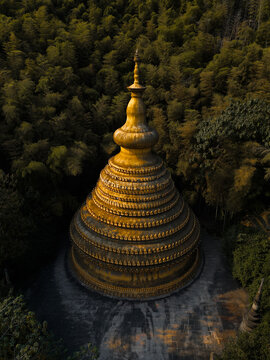 Aerial view of a golden pagoda emerges from the deep green forest, its tiered structure glowing against the dark foliage, Hangzhou, Zhejiang, China.
