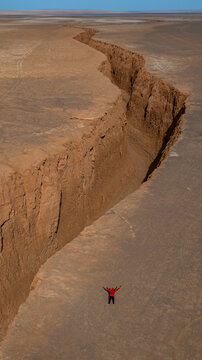 Aerial view of a dramatic chasm cleaves through the ochre earth, a lone figure stands silhouetted against the stark beauty of the arid landscape, Shahdad, Kerman Province, Iran.