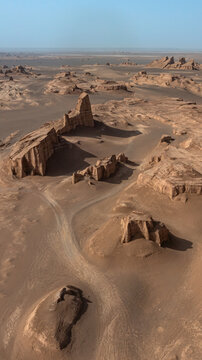 Aerial view of wind-sculpted yardangs rise majestically from the sun-baked desert floor, casting long shadows under the clear sky, Shahdad, Kerman Province, Iran.