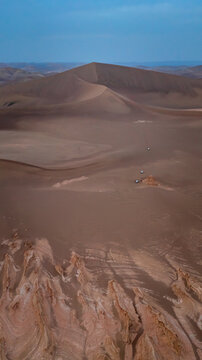Aerial view of the stark, arid landscape unfolds, revealing towering sand dunes and jagged rock formations under the fading light, Shahdad, Kerman Province, Iran.