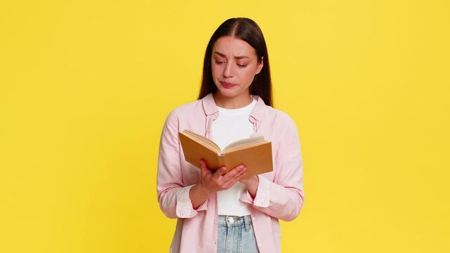 Young woman reading book with wide open eyes amazed expression, deeply intrigued by thrilling and surprising plot. Girl on yellow background emotionally reacts to intense captivating story development
