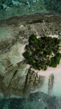 Rocky coastline with small tropical island covered in coconut trees surrounded by blue sea water. Siargao, Philippines.