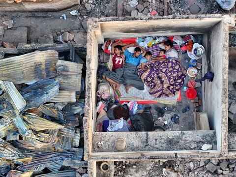 Dhaka, Bangladesh - 28 November 2025: Aerial view of a family seeking refuge in a concrete structure amidst the stark, charred remains of the Korail slum.