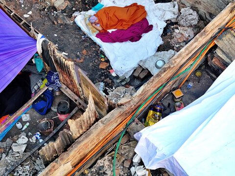 Dhaka, Bangladesh - 28 November 2025: Aerial view of the Korail slum with vibrant colored fabrics strewn across weathered rooftops, a stark contrast against the rugged landscape.