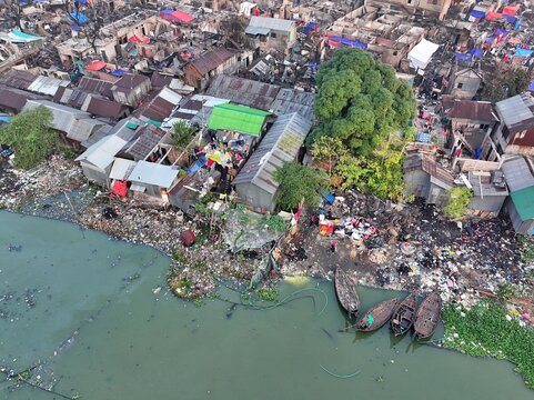 Dhaka, Bangladesh - 28 November 2025: Aerial view of the Korail slum's chaotic landscape, where ramshackle dwellings meet a riverbank choked with debris under a hazy sky.