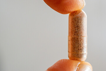 Red rice tablet capsule between the thumb and index finger in macro photography.