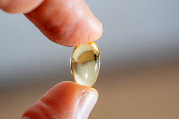 Omega-3 capsule tablet placed between the thumb and index finger in macro photography.