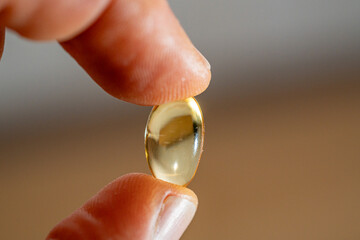 Omega-3 capsule tablet placed between the thumb and index finger in macro photography.