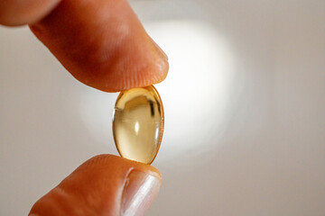 Omega-3 capsule tablet placed between the thumb and index finger in macro photography.