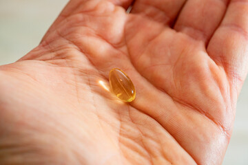 Omega 3 translucent capsule tablet over human hand palm, white person.