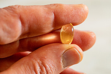 Omega-3 capsule tablet placed between the thumb and index finger in macro photography.