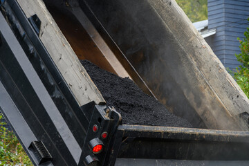 Roadworks construction, dump truck with fresh hot smokey asphalt and raised be dumping paving materials

