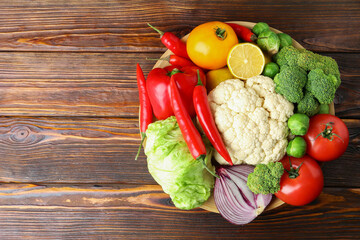 Different fresh raw vegetables and fruits in bowl on wooden table, top view. Space for text
