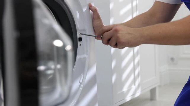 Repairman fixing broken washing machine with screwdriver at home, closeup. Camera moving forward