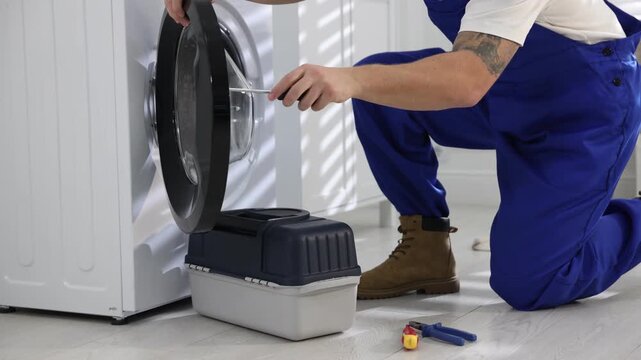 Repairman fixing broken washing machine with screwdriver at home, closeup. Camera moving forward