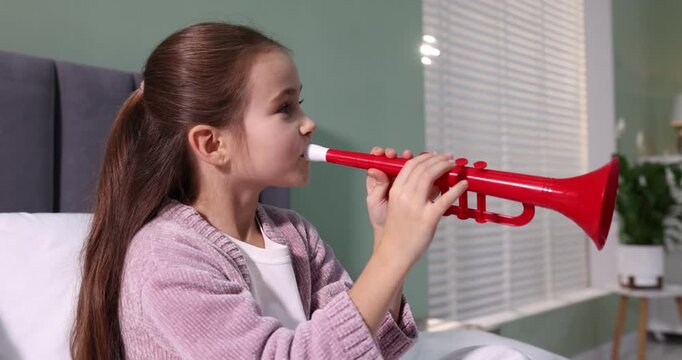 Little girl playing toy trumpet on bed at home