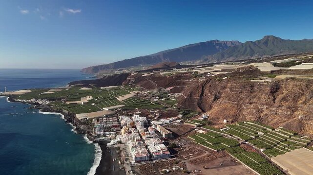 High altitude aerial drone flyover showing the entire popular tourist resort of Puerto Naos and its unique black volcanic sand beach on La Palma, Canary Islands, Spain.